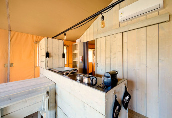 Coin cuisine d’une tente safari avec des murs en bois clair, appareils électroménagers et climatisation.