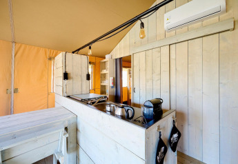 Køkkenområde i et safaritelt med lyse træpaneler, apparater, ophængte lamper og aircondition.