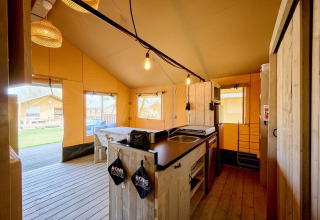 Interiør af et luksuriøst safaritelttelt med køkken, spisebord og udsigt til terrasse og grønne områder.