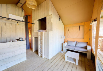 Interior of a Villatent Cottage safari tent showing light wooden decor, small lounge, and sleeping loft.
