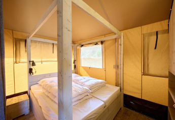 Innenansicht eines Safarizeltes mit gemütlichem Doppelbett, Holzrahmen und weichem Licht.