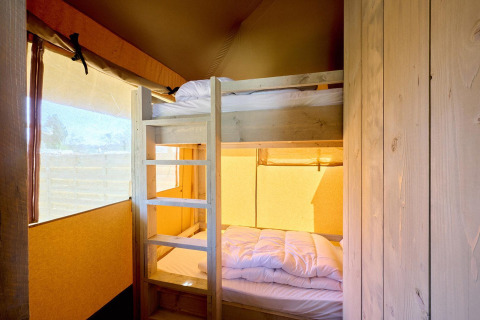 Interieur van een safaritent met houten stapelbedden en zacht daglicht door grote ramen in de slaapkamer.