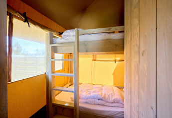Interior view of a safari tent bedroom featuring bunk beds and soft daylight streaming through windows.