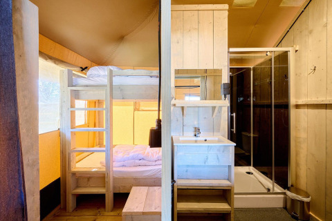 Innenansicht eines Safarizeltes mit Etagenbett, Waschbecken und moderner Dusche aus hellem Holz.