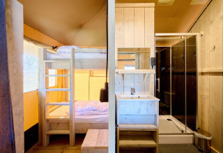 Billedet viser indretningen af et safaritelt med køjeseng, håndvask og brusebad i lyst træ.