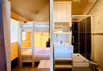 Interior of a safari tent featuring a wooden bunk bed, sink, and a modern enclosed shower area.