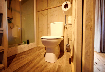 Badeværelse i safaritelt med moderne toilet, trævægge, brusekabine og trægulv med naturligt lys.