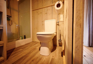 Bathroom in a safari tent featuring a modern toilet, wood paneling, shower, and natural wood flooring.