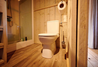 Badeværelse i safaritelt med moderne toilet, trævægge, brusekabine og trægulv med naturligt lys.