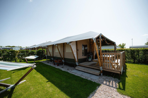 Lodge Villatent Cottage en Camping de Molenhoek, Países Bajos, con terraza de madera y hamacas en el césped.