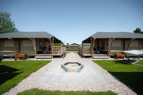 Due lodge Villatent Cottage al Camping de Molenhoek nei Paesi Bassi con prato, camino e carrellini rossi.