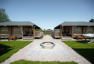 Due lodge Villatent Cottage al Camping de Molenhoek nei Paesi Bassi con prato, camino e carrellini rossi.