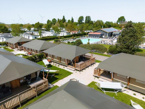 View of Villatent Cottage at Camping de Molenhoek in the Netherlands, featuring tents, pool, and greenery.