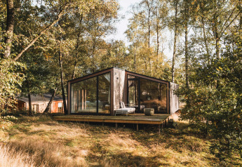 Moderne Holzhütte mit großen Fenstern im Wald bei Wilsumer Berge, Deutschland, von Bäumen umgeben.