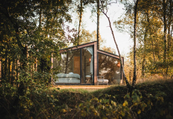 Cabaña moderna de cristal, Cabin on the Hill, en Wilsumer Berge, Alemania, rodeada de árboles y naturaleza.