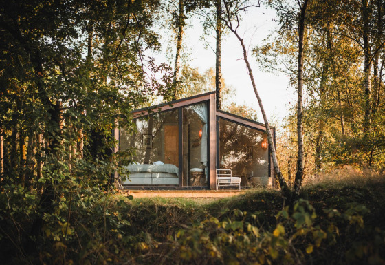 Cabane moderne en verre, Cabin on the Hill, à Wilsumer Berge, Allemagne, entourée d'arbres en pleine nature.