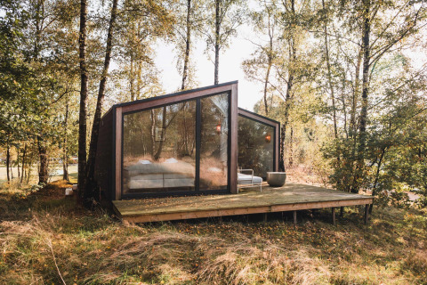 Moderne kabine med store glasvinduer i en skov ved Wilsumer Berge, Tyskland, set fra en træterrasse.
