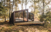 Moderne kabine med store glasvinduer i en skov ved Wilsumer Berge, Tyskland, set fra en træterrasse.