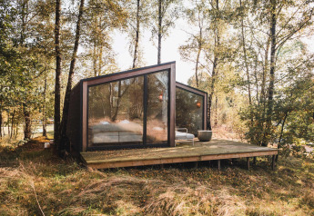 Moderne kabine med store glasvinduer i en skov ved Wilsumer Berge, Tyskland, set fra en træterrasse.
