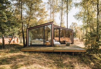 Cabina moderna con grandi finestre in vetro su una terrazza in legno nella foresta, Wilsumer Berge, Germania.