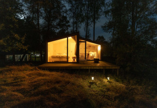 Cabaña iluminada en la colina de Wilsumer Berge, Alemania, rodeada de árboles y fotografiada de noche.
