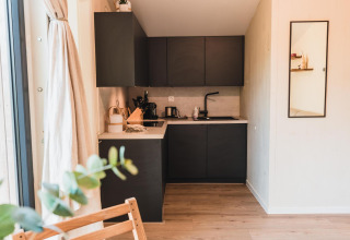 Moderne keukenhoek in Cabin on the Hill, Wilsumer Berge, Duitsland, met zwarte kasten en houten vloer.