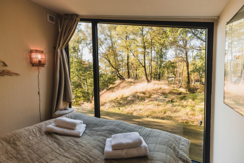 Vista dalla camera da letto di Cabin on the Hill a Wilsumer Berge, Germania, con grandi vetrate sul bosco.