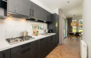Modernes Lodge-Kücheninterieur mit dunklen Schränken, Gasherd und Essbereich mit Blick ins Grüne.
