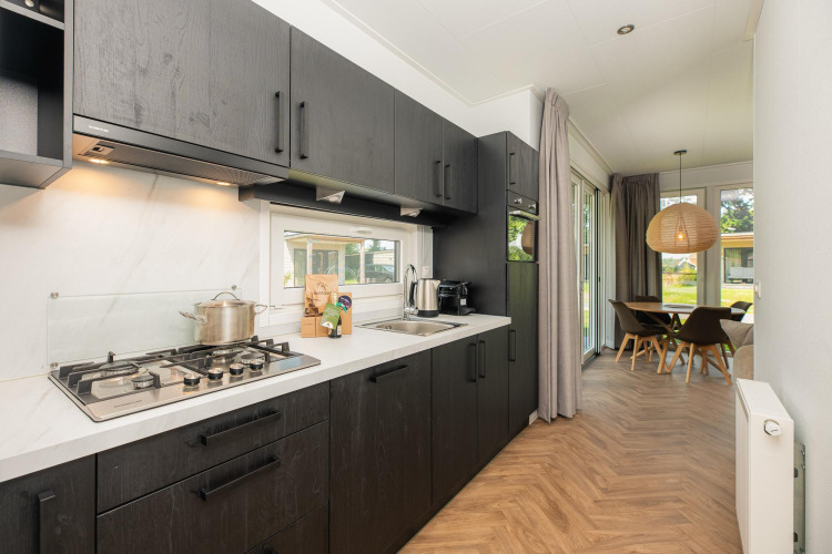 Contemporary lodge kitchen with dark cabinets, gas stove, dining area, and large windows overlooking garden.
