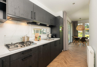 Modernes Lodge-Kücheninterieur mit dunklen Schränken, Gasherd und Essbereich mit Blick ins Grüne.