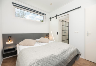 Modernes Lodge-Schlafzimmer mit Doppelbett, grauer Tagesdecke und Zugang zum Badezimmer mit Dusche.