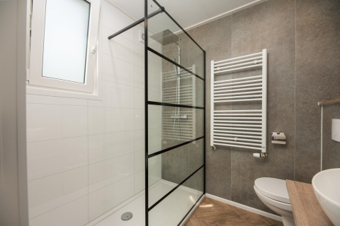 Baño moderno de lodge con mampara de ducha de vidrio, radiador toallero y tocador de madera clara.