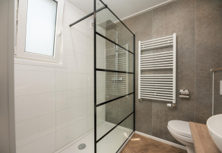 Bagno moderno di lodge con parete doccia in vetro, termoarredo bianco e lavabo su piano in legno.