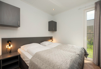 Modernes Lodge-Schlafzimmer mit Doppelbett, grauen Schränken, Nachttischlampen und Gartenausblick.