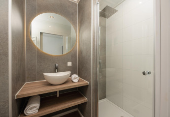 Modern lodge bathroom with round mirror, vessel sink, wooden shelves, and glass-enclosed shower area.
