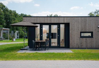 Moderne lodge med træbeklædning, udendørs terrasse, parasol og spisebord på en grøn græsplæne.