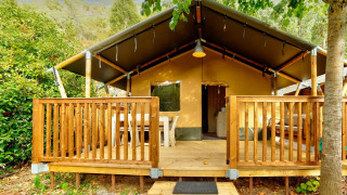 Tienda safari con terraza de madera en Camping Delle Rose, rodeada de árboles, Villatent Outback, Italia