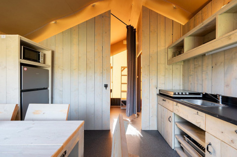 Interieur van een Villatent Outback safaritent met keuken, eettafel en zicht op het slaapgedeelte.