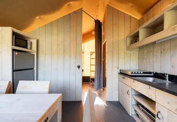 Interno di una tenda safari Villatent Outback con cucina, tavolo da pranzo e vista verso la zona notte.