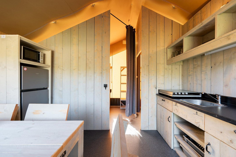 Interior de una tienda safari Villatent Outback con cocina, mesa de comedor y acceso al área de dormitorios.