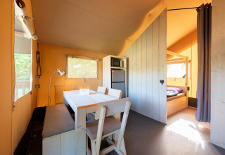 Interior de tienda safari Villatent Outback con comedor, cocina pequeña, refrigerador y zona de dormir.