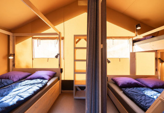 Binnenkant van een safaritent Villatent Outback met twee bedden, stapelbed en zonlicht via de ramen.