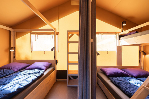 Binnenkant van een safaritent Villatent Outback met twee bedden, stapelbed en zonlicht via de ramen.