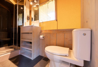 Baño en tienda safari Villatent Outback con inodoro, ducha, espejo y acabados en madera clara.