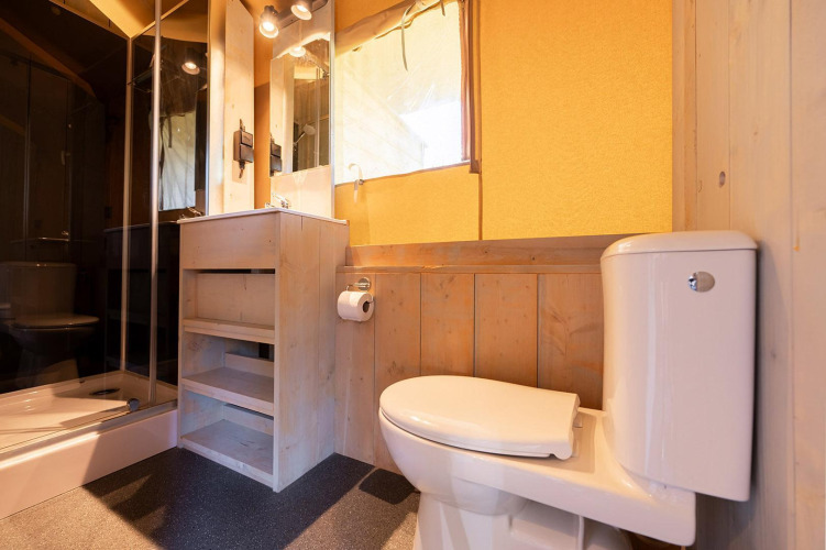 Baño en tienda safari Villatent Outback con inodoro, ducha, espejo y acabados en madera clara.