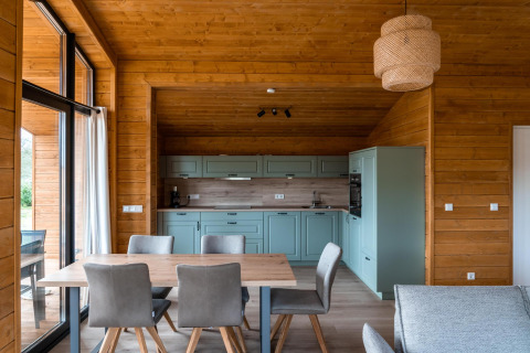 Intérieur de chalet moderne en bois avec cuisine ouverte, coin repas et grandes fenêtres à Lakehouse Scandi, Wilsumer Berge.