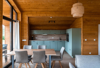 Moderne træhytteinteriør med åbent køkken, spisebord og store vinduer i Lakehouse Scandi, Wilsumer Berge.