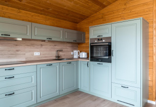 Moderne keuken met groene kasten en houten wanden in Lakehouse Scandi, Wilsumer Berge, Duitsland.