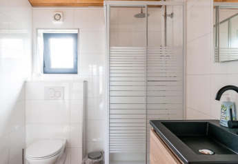 Baño moderno en Lakehouse Scandi, Wilsumer Berge, Alemania, con ducha acristalada y lavabo negro.