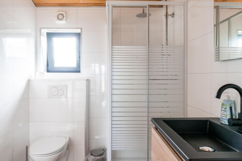 Baño moderno en Lakehouse Scandi, Wilsumer Berge, Alemania, con ducha acristalada y lavabo negro.